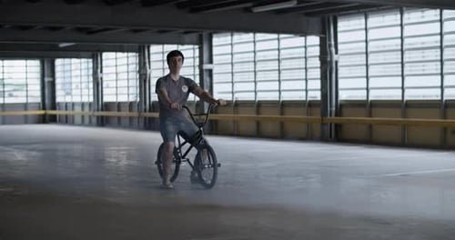 Male Professional BMX Rider Sitting on Bike in Parking Lot