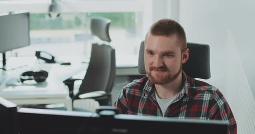Ein junger bärtiger Mann sitzt am Computer, arbeitet im Büro, fühlt sich glücklich, Kollege, Unternehmenskonzept