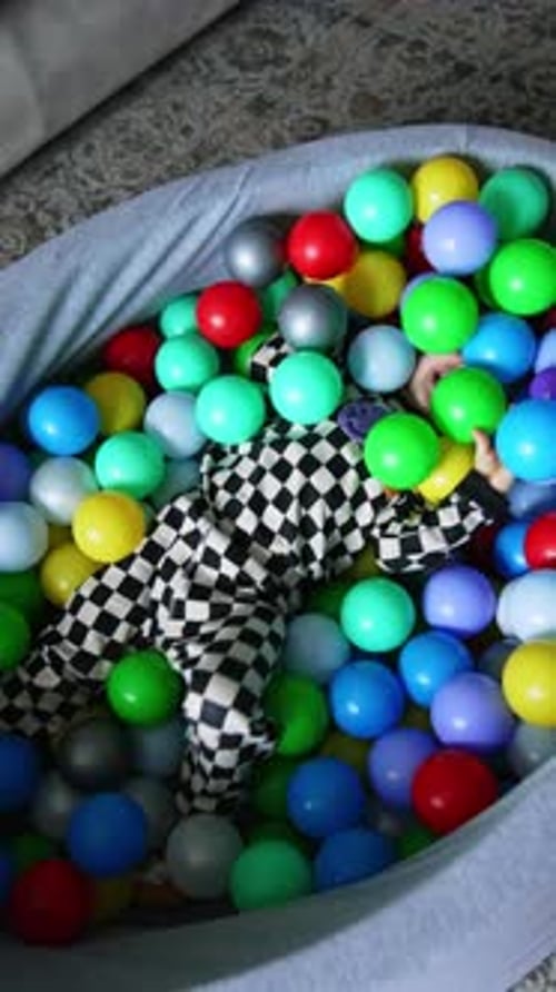 Joyful energetic toddler boy tumbles in the dry pool among the colorful balls.