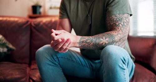Man with Tattoos Sits Contemplatively on Sofa