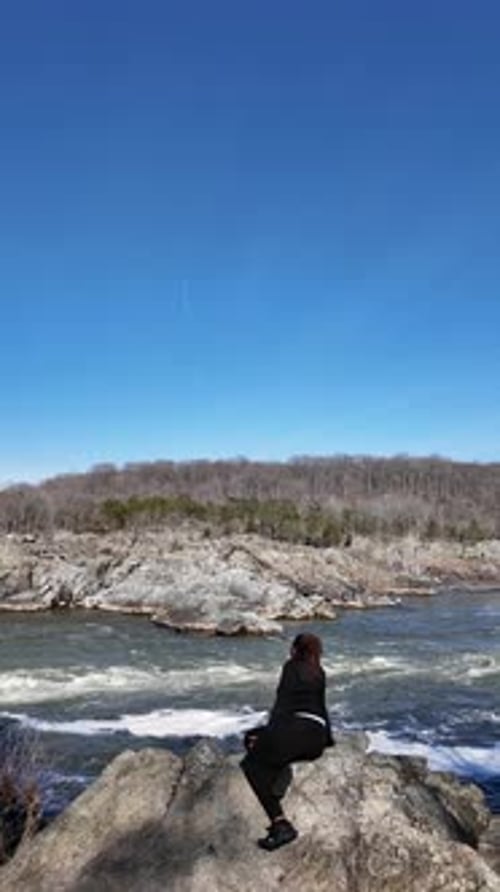 Vertical view of woman on rocky cliff by flowing mountain river