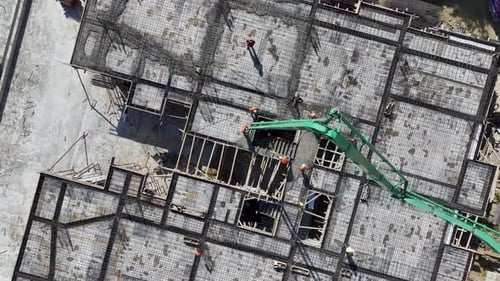 Vista aérea: trabajadores de la construcción vertiendo concreto y dando forma a barras de refuerzo para una estructura