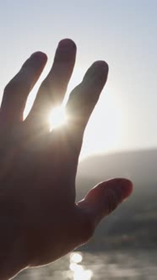 Hand Reaching Towards Sunlight at Ocean Shoreline