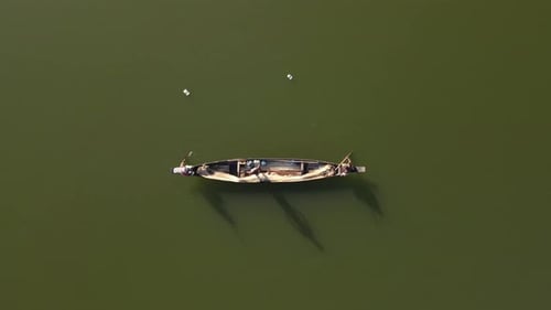 Top down aerial shot of a small wooden boat in a lake and fishermen catching fish with net in tradit