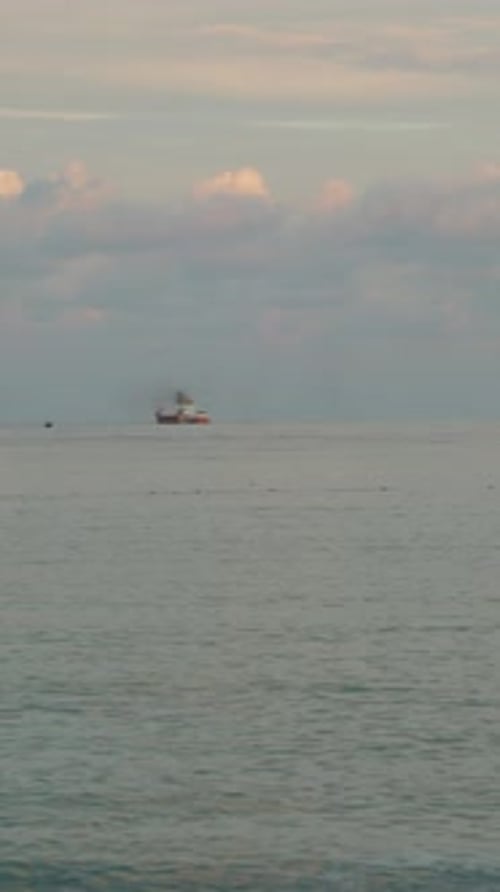Vertical video. Panorama of the Bay in the Sea between Two Rocks, a Ship in the Distance at Sunset.