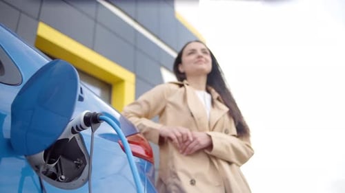 Woman Leans on Electric Car While Charging