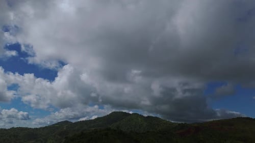 Dense clouds moving over the forested hills during the day covering blue sky