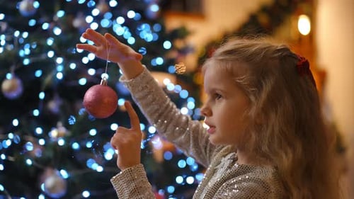 Child Decorates Christmas Tree with Pink Ornament