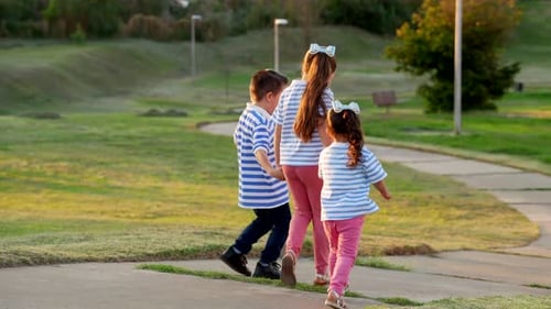 Three mexican latino friends sibling boys running down the path in a park outside outdoors playing