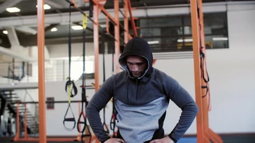 Young Sportsman in Hoodie and Hood is Resting Breathing Deeply in Gym