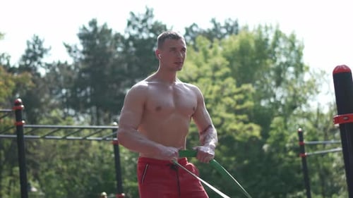 Muscular Man Exercising with Resistance Band Outdoors