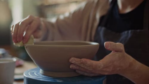 Close Up of Ceramist Smoothing Edge of Clay Bowl with Sponge on Pottery Wheel