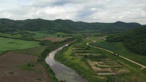 Sliding aerial footage towards the right revealing an awesome landscape, canal, farmlands, dirt road