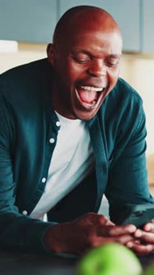 Man Laughing While Looking at His Phone Indoors