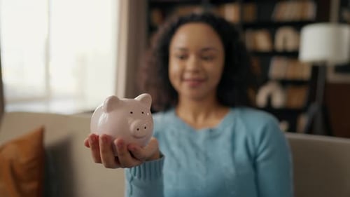 Junges Mädchen spart Geld für einen Traum, eine afroamerikanische Teenagerin, die eine Münze in ein rosafarbenes Schweinchen wirft