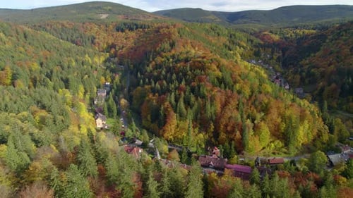Aerial establishing shot of the beautiful village hidden in the mountain forest in autumn