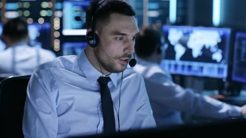 In System Control Center Technical Support Specialist Speaks into Headset. His Colleagues are Worki