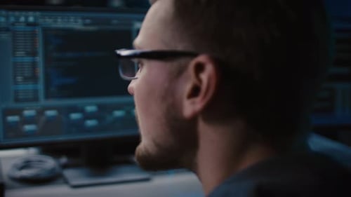 Retrato de especialista em TI usando óculos funciona em computador pessoal com telas mostrando software