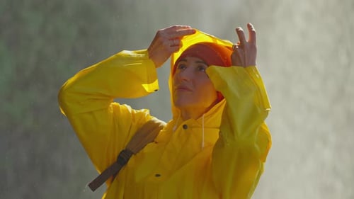 Portrait of a Girl in a Yellow Raincoat Standing Under the Spray of a Waterfall Putting on a Hood to