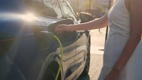 Woman Plugging in Electric Car on City Street