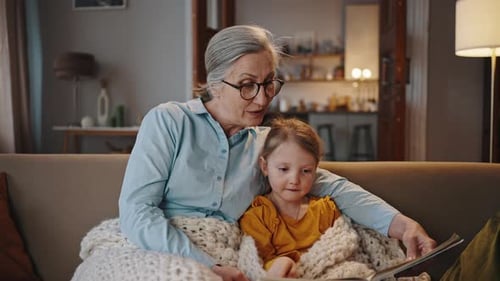 Grandmother Reads Book to Child on Sofa