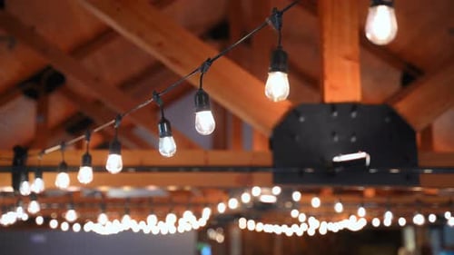 Glowing Bulbs Strung Across Beams in a Rustic Event Hall Radiating Warm Golden Light and Festive