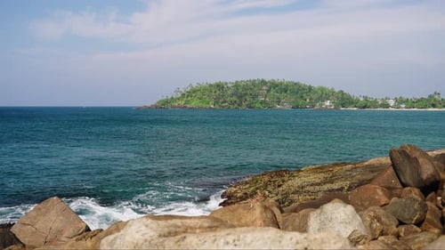 Clear Blue Ocean Gently Laps Tropical Coast Serene Maritime Scene with Waves Boulders Foreground