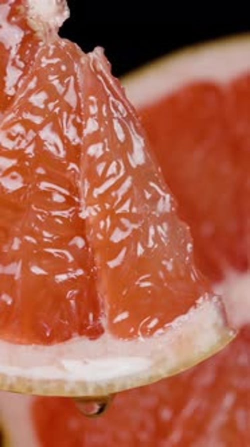 Vertical video. In slow motion, juice is dripping from a grapefruit wedge. Close-up of the red juicy