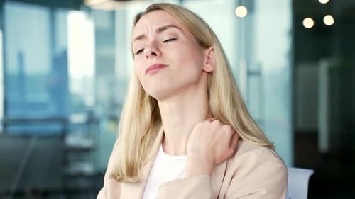 Close up. Tired blonde businesswoman suffering from neck pain while sitting at workplace in modern