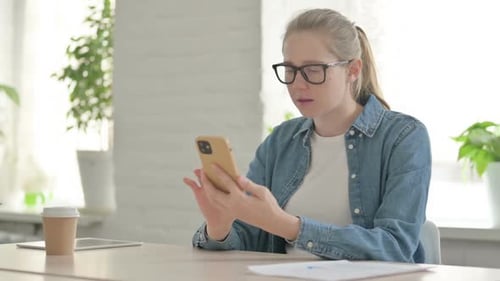 Shocked woman uses mobile phone at desk