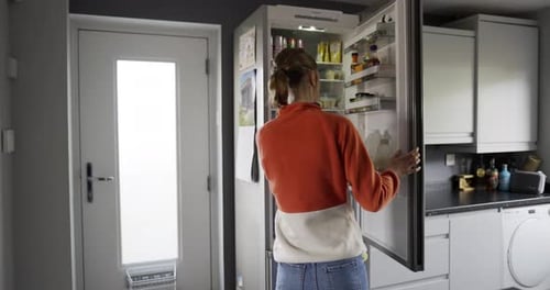 British Woman opening a fridge door in a kitchen