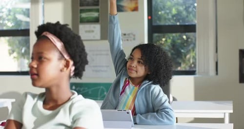 Classmates African American teen female in hoodie raising right hand while using tablet to answer