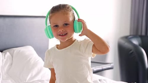 Portrait of Little Girl Listening Music with Green Kids Headphones in Home Bed