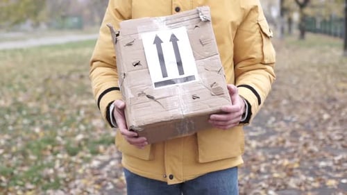 Man Holds Damaged Shipping Box Outdoors in Park