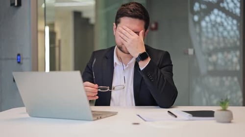 Tired Businessman with Headache Massaging Temples at Desk