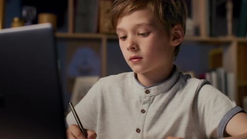Child Studying, Writing in Notebook Near Laptop at Desk