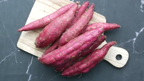 Primer plano de batata cruda sobre tabla de cortar sobre fondo negro