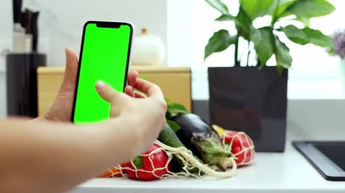 Close-up of female hands holding smartphone with green screen on a background of organic vegetables