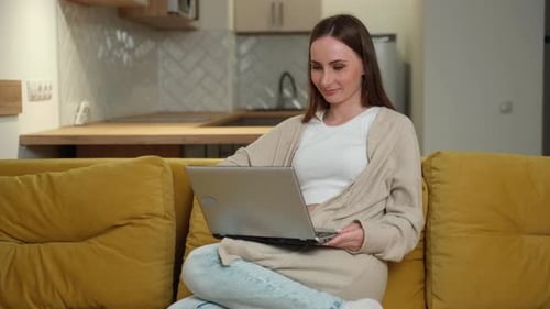 Woman Opens Laptop on Yellow Couch Indoors