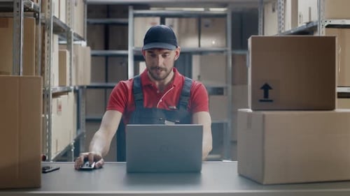 Worker Uses Laptop while Sitting at His Desk in the Warehouse.