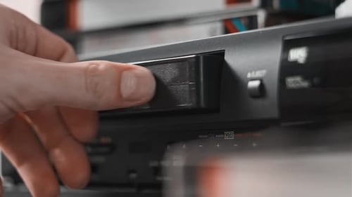 Male Hand Inserts VHS Cassette Into a VCR Video Recorder