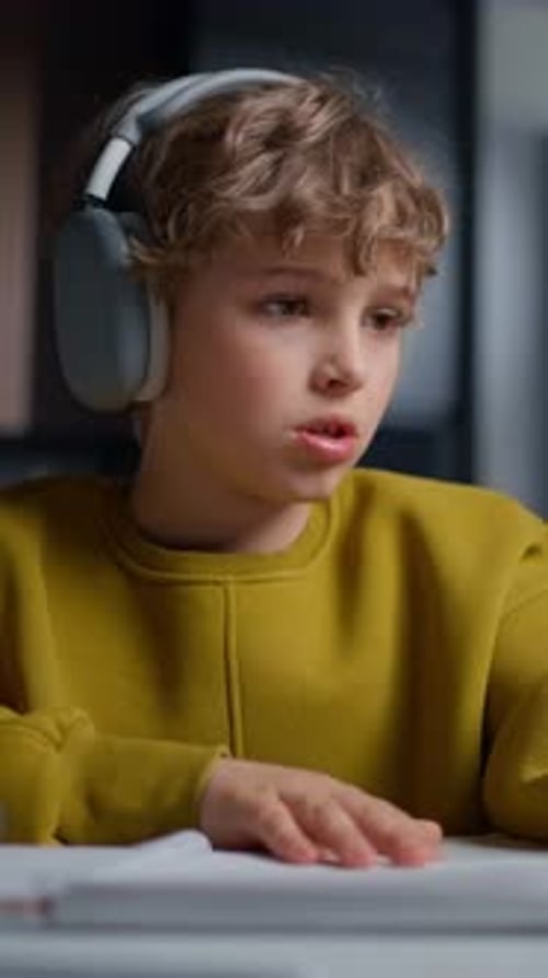 Focused Young Boy Wearing Headphones and a Mustard Yellow Sweater Diligently Writing in a Notebook