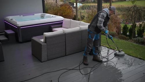 Man Cleans Patio Area Near Hot Tub Outdoors with Pressure Washer