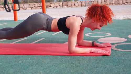 Determined Sporty Woman Doing Plank Exercise on Mat at Outdoor Gym
