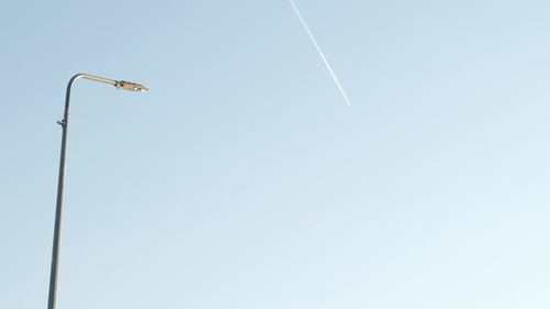 Plane trail against a clear blue sky with a lamppost