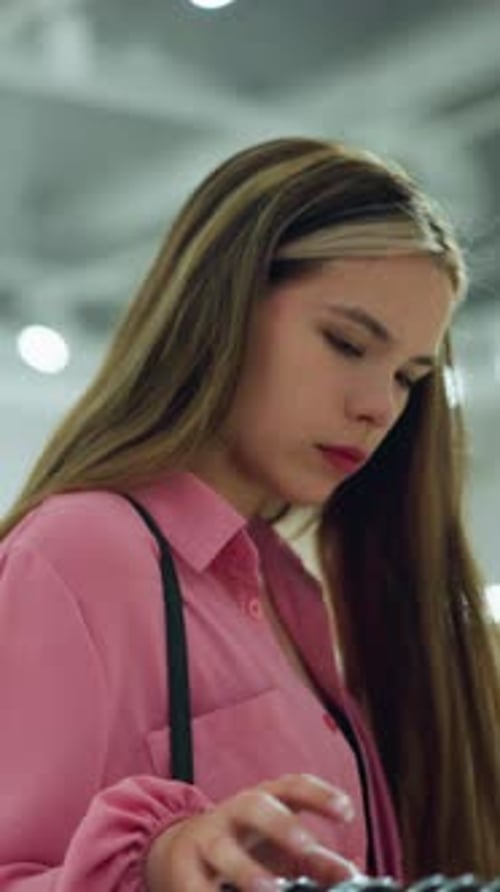 Jeune femme en haut rose avec sac à main naviguant pensivement dans Bright Mall