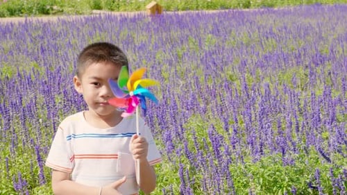 Smiling Little Boy Holds a Toy Pinwheel in a Flower Garden Spring Brings Joy and Freedom Wind Spins