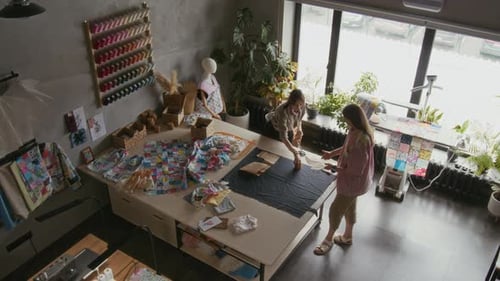 Top view of Two Female Tailors Laying Out Patterns on Fabric on Cutting Table