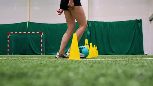 young girl is training on the soccer field driving the ball between the chips or cones for the match