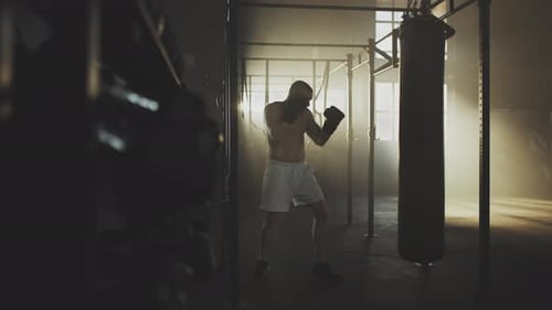 Muscular Boxer Punches Heavy Bag in Dark Gym
